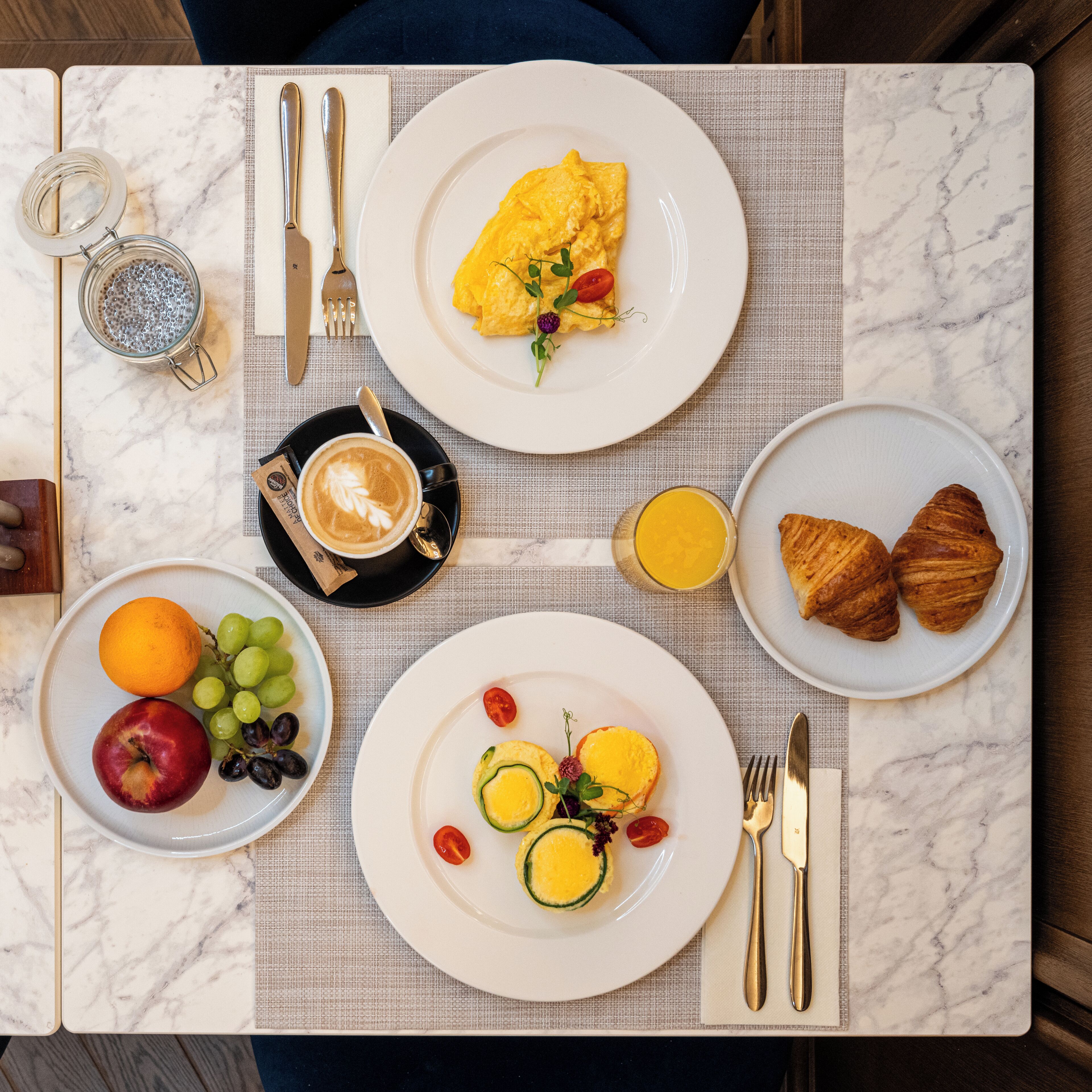 A breakfast setting with plates of food, a coffee cup, and a glass of juice on a marble table.