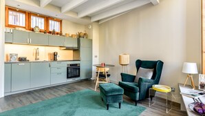 Una cocina moderna con armarios verde claro, techo de madera y un comedor con un sillón y reposapiés verdes.