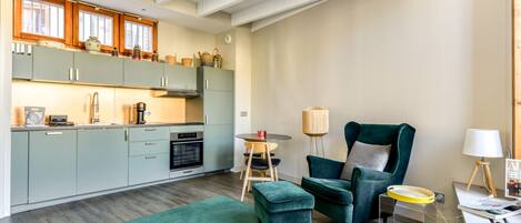 A modern kitchen with light green cabinets, a wooden ceiling, and a dining area with a green armchair and ottoman.