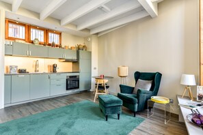 Eine moderne Küche mit hellgrünen Schränken, einer Holzbalkendecke und einem Essbereich mit einem grünen Sessel und Hocker.