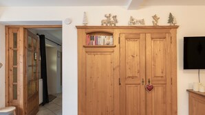 A wooden wardrobe with a heart-shaped decoration, a bookshelf above it, and a television on the wall. - Cosy Apartment “La Tanière” in Saint-Gervais-les-Bains (Saint-Gervais-les-Bains)