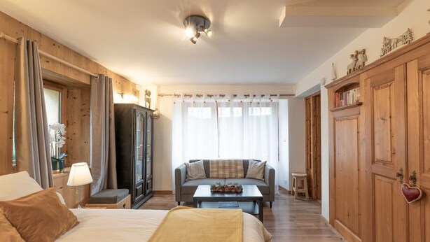 A hotel room with a bed, a sofa, a small table with fruit, a cabinet, and a door with a heart-shaped decoration. - Cosy Apartment “La Tanière” in Saint-Gervais-les-Bains (Saint-Gervais-les-Bains)
