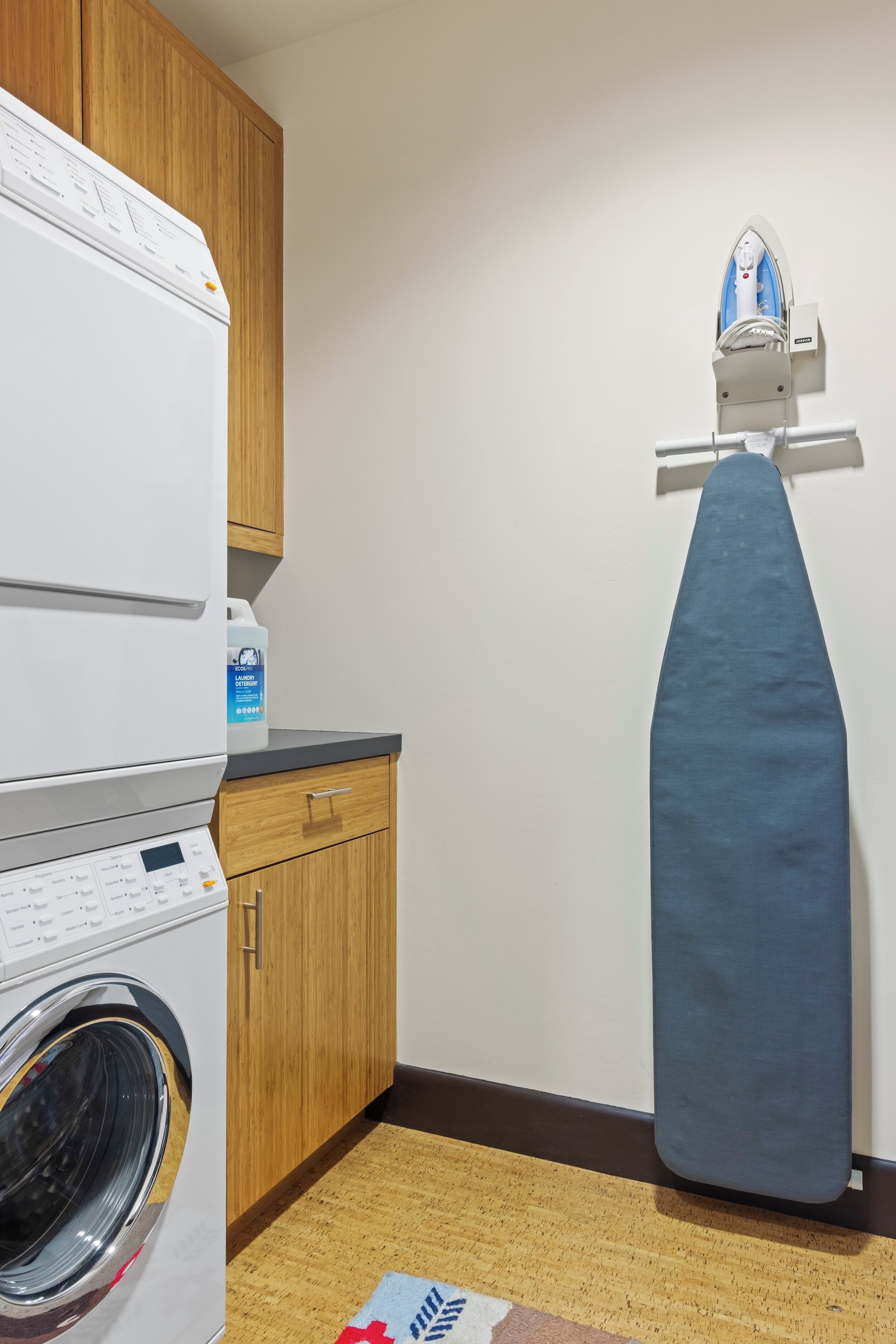 A laundry area with a washing machine, a drying rack, and a detergent bottle.