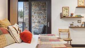 Ein Schlafzimmer mit Bett, Stuhl, einer Holzhülle mit Büchern und einer Vase, sowie einer Steinsäule.