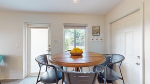 Een eethoek met een ronde houten tafel, vier stoelen, een raam met luiken en een deur.