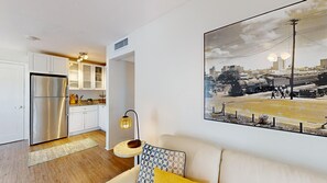 Een moderne keuken met witte kastjes, een roestvrijstalen koelkast en een stadsgezichtschilderij aan de muur.