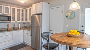 A modern kitchen with white cabinets, a stainless steel refrigerator, a wooden dining table with a bowl of lemons, and a pendant light. - 2BR • 4 Beds • by Miami SoFi Vacation Rentals <br>Tucked in a quiet Palmetto Bay neighborhood, this property offers stylish 2BR/1BA stays with thoughtful design, outdoor spaces, and easy access to parks, dining, and Miami hotspots. (Palmetto Bay)