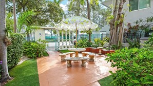 A courtyard with a central table and chairs, surrounded by lush greenery and a white umbrella. - Bright SoFi 1BR, with queen bed, 1 bath, and FREE parking—rare for South Beach.  <br>Walk to South Pointe Park, the beach, top dining, and nightlife.  By Miami SoFi Vacation Rentals. (Miami Beach)