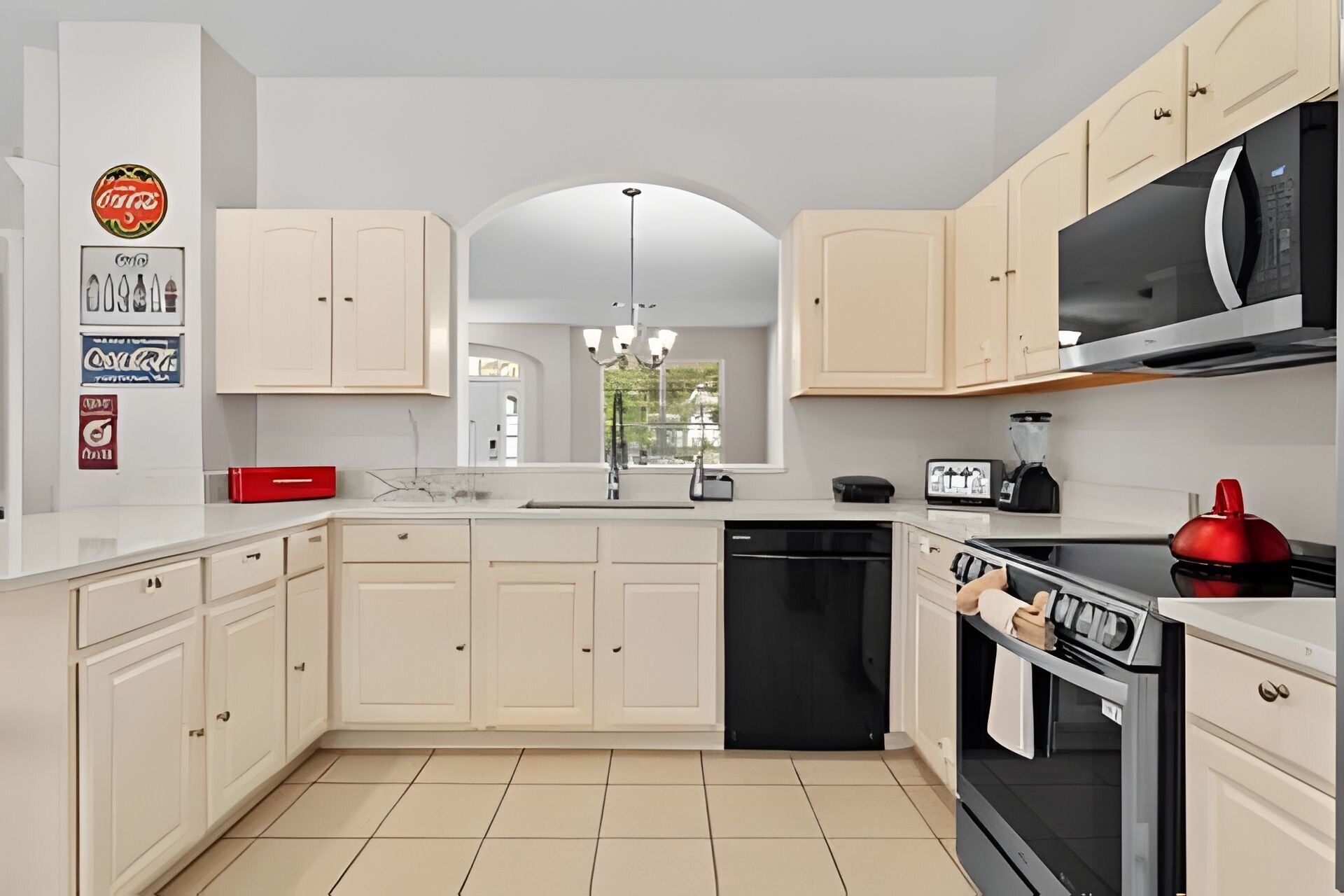 A modern kitchen with white cabinets, a black dishwasher, a red kettle, and a microwave.