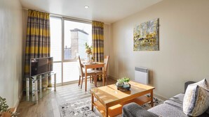 A modern living room with a glass coffee table, a sofa, a TV on a glass stand, and a dining area with a table and chairs. - Host Stay 408 Hatton Garden (Liverpool)