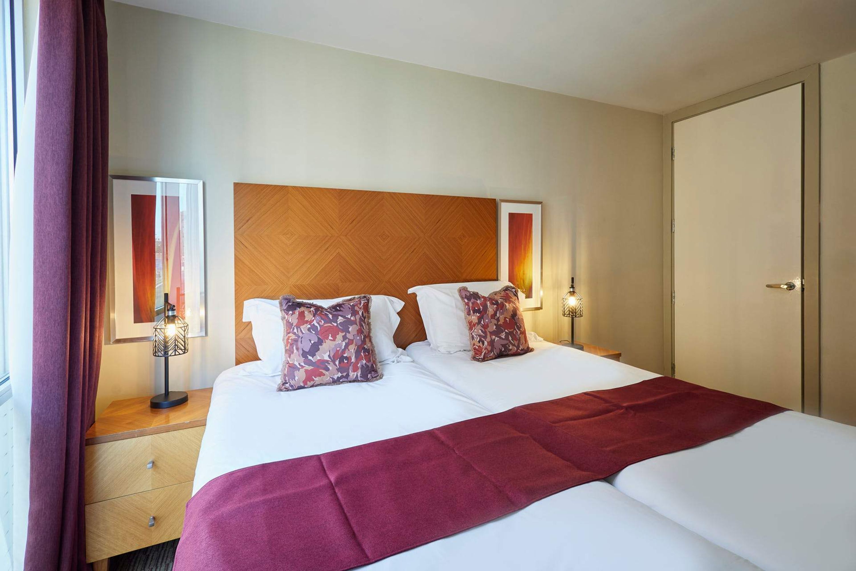 A hotel room with a large bed, two bedside tables, a wooden headboard, and a door.