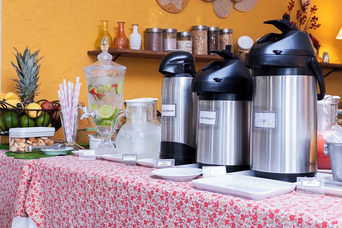 Una mesa con cafeteras, un frutero y dispensador de agua.