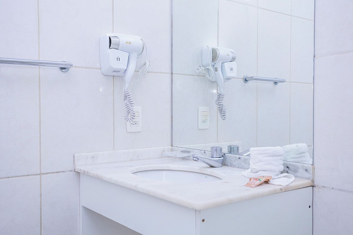 A bathroom with a white sink, two hair dryers mounted on the wall, a towel rack, and a mirror.