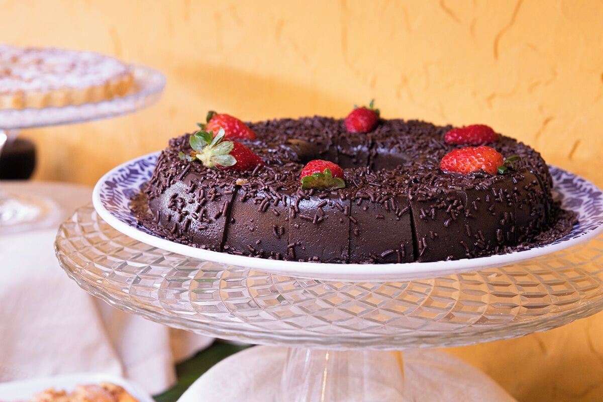 A chocolate cake with strawberries on a glass cake stand.