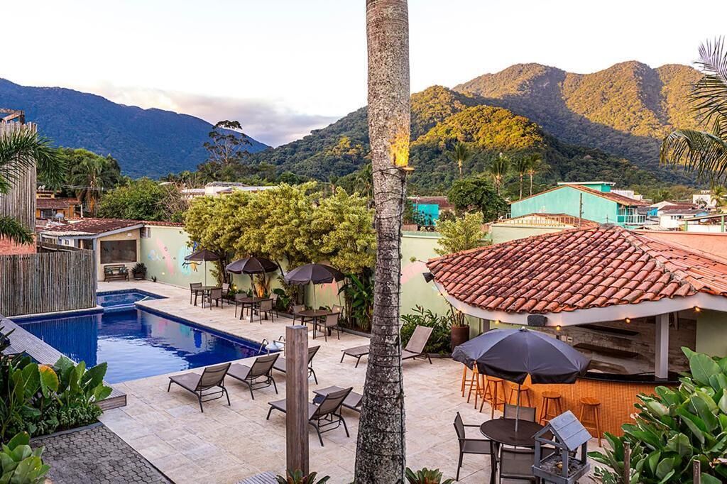 A pool area with lounge chairs and umbrellas, surrounded by greenery and buildings with red-tiled roofs.
