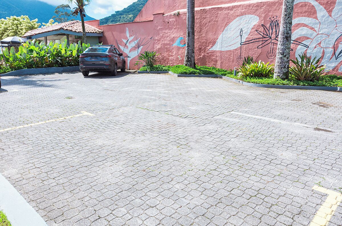 Un estacionamiento pavimentado con un automóvil estacionado, un mural en la pared y vegetación circundante.