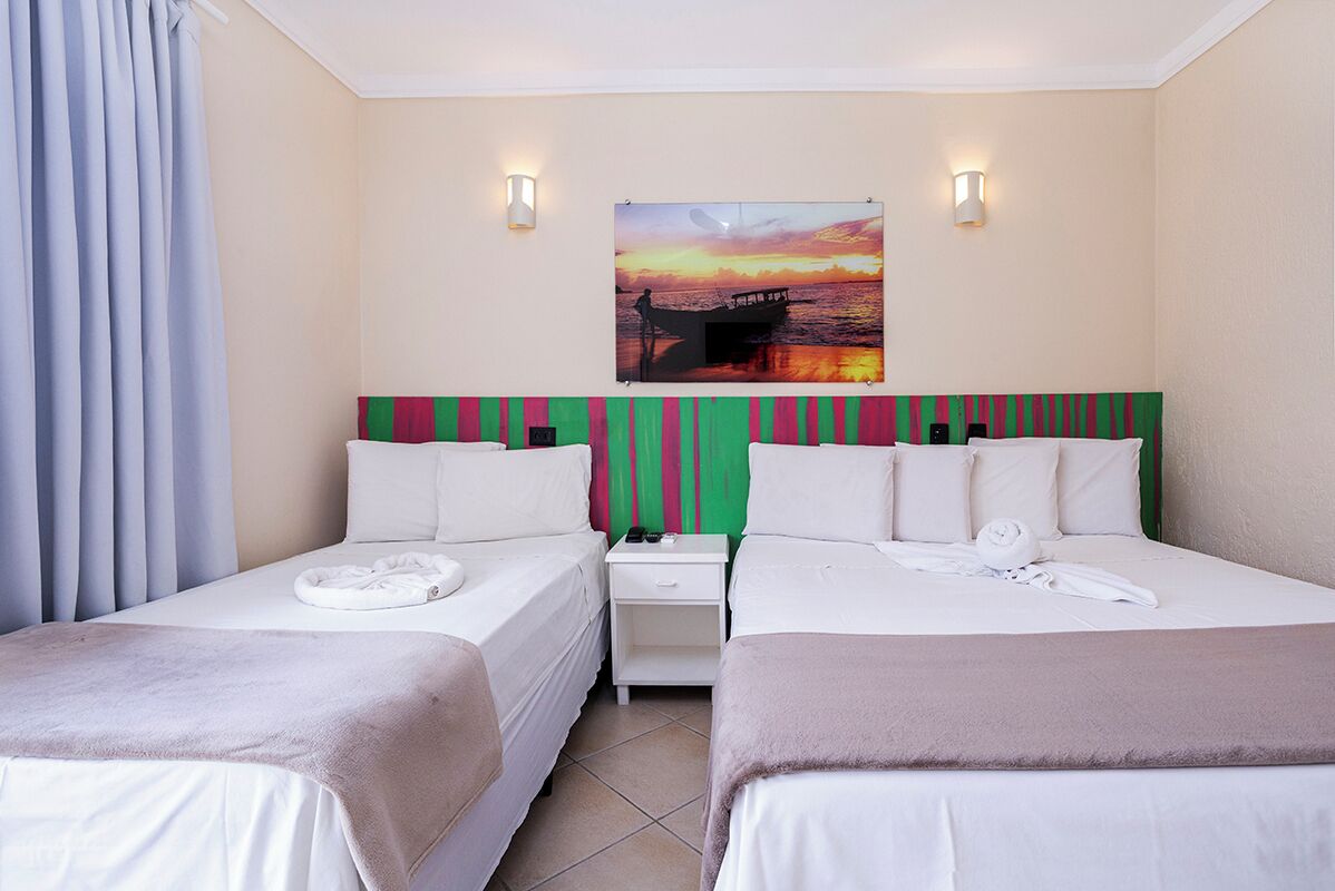 Une chambre d’hôtel avec deux lits, un tableau représentant un coucher de soleil sur l’eau et deux lampes de chevet.