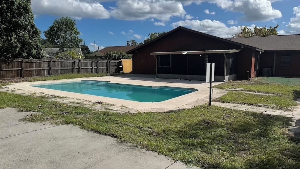 Un jardin avec une piscine rectangulaire, un patio couvert et une maison avec un garage.