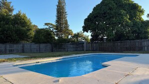 Une piscine rectangulaire avec une plage en béton, entourée d’une clôture en bois et d’arbres.