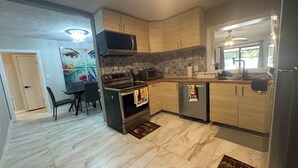 Une cuisine moderne dotée d’un îlot central, d’un micro-ondes, d’un four et d’un lave-vaisselle encastrés. On y trouve également un coin repas avec une table et des chaises, ainsi qu’un tableau abstrait aux couleurs vives accroché au mur.