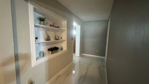 Un couloir avec un mur blanc, une pancarte indiquant « Bienvenue » et un sol en marbre.