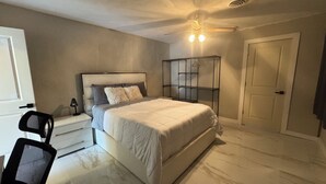Une chambre à coucher comprenant un lit, une table de chevet, une chaise, un bureau, une armoire et un ventilateur de plafond.