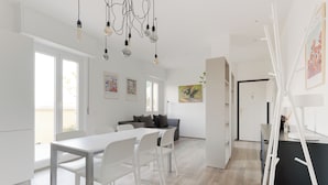 A modern, well-lit living area with a dining table, chairs, a sofa, and a kitchen area. - Brera Apartments Navigli (Milan)