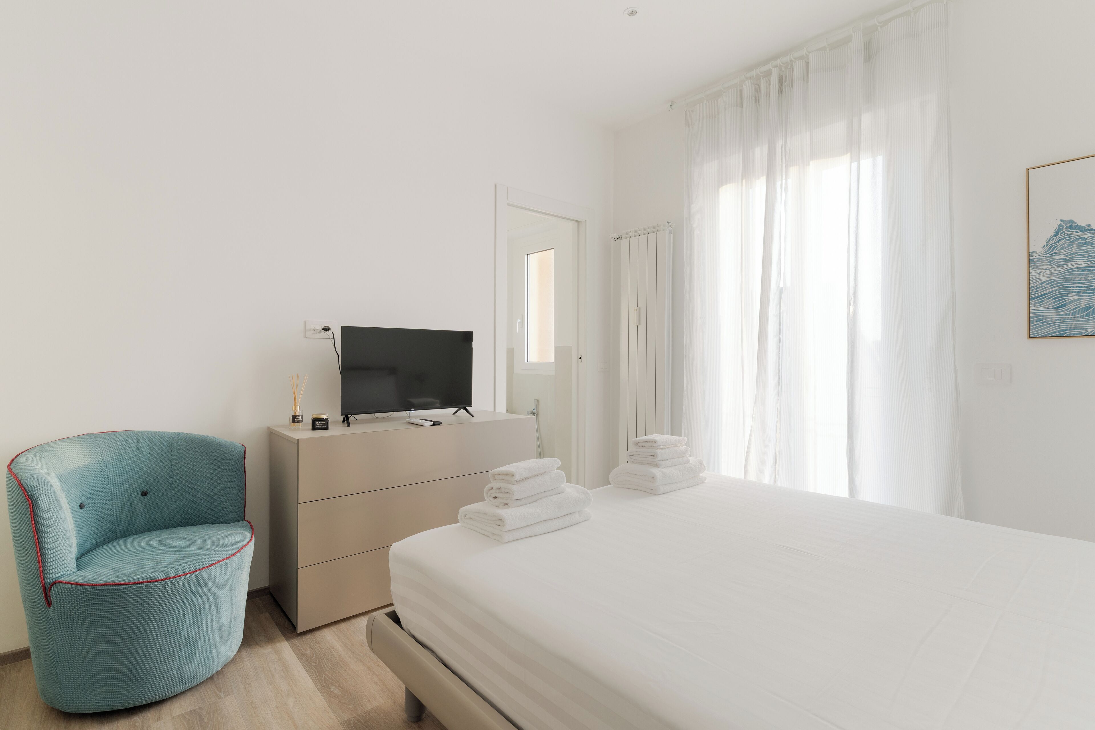 Ein Hotelzimmer mit einem Bett, einem Fernseher auf einer Kommode, einem Sessel und einem Fenster mit Vorhängen.