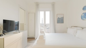 A modern hotel room with a bed, a TV on a dresser, a window with curtains, and a city view. - Brera Apartments Navigli (Milan)