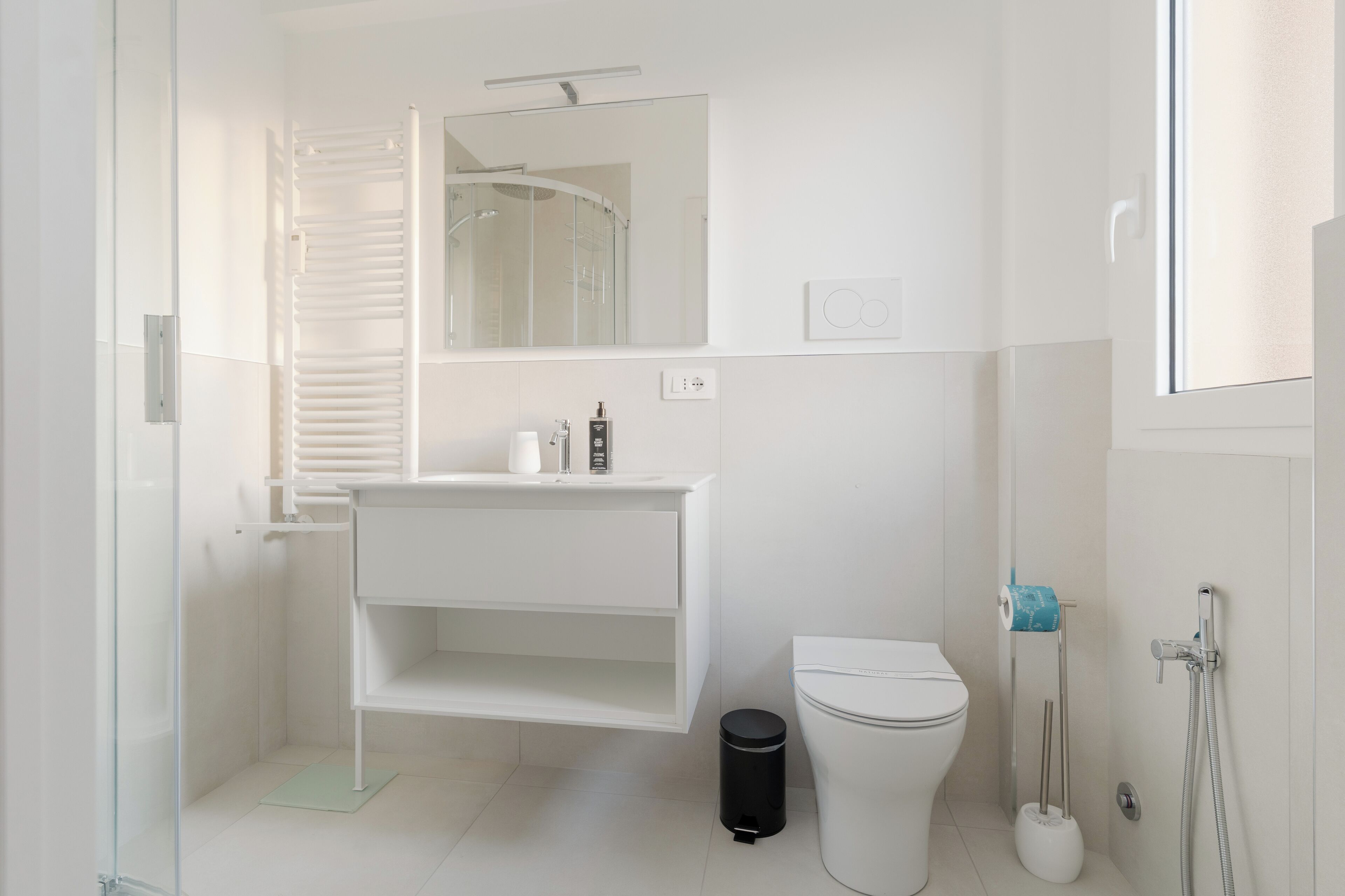 Une salle de bain moderne avec une douche à parois de verre, des toilettes blanches et un lavabo avec un miroir au-dessus.