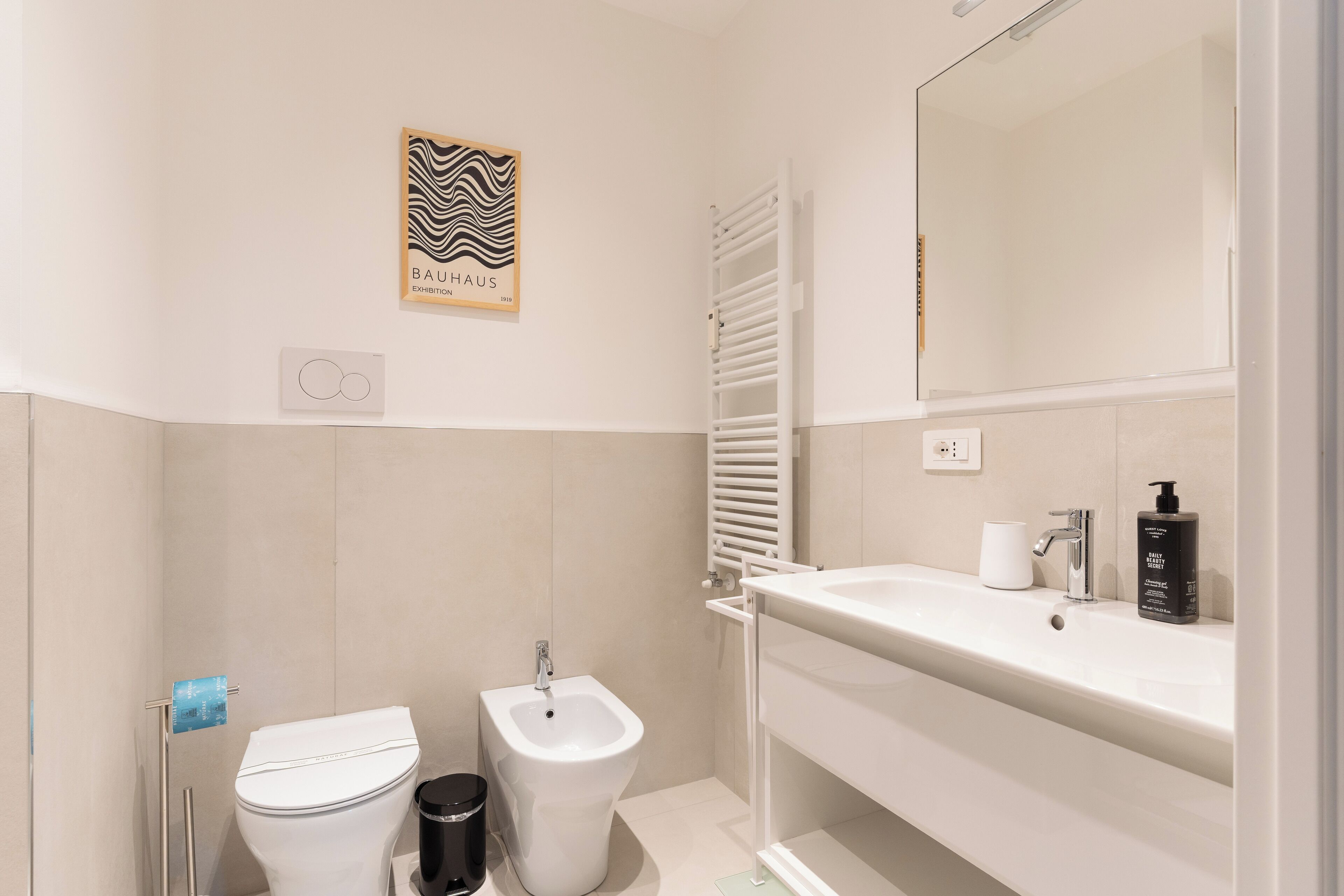 A modern bathroom with a bidet, toilet, and a large mirror above the sink.
