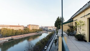 A riverside view with a row of parked cars, a bridge, and buildings in the background. - Brera Apartments Navigli (Milan)