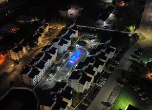 An aerial view of a residential area with multiple white buildings, a swimming pool with blue lighting, and a parking lot. - Big Buoys On The Lake (Osage Beach)