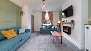 Un salon avec un canapé de couleur turquoise, une table basse, une cheminée et un téléviseur fixé au mur.