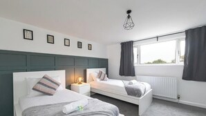 Ein Schlafzimmer mit zwei Betten, einem Fenster mit Vorhängen, einem Heizkörper und gerahmten Bildern an der Wand.