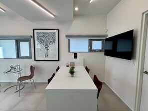 A modern conference room with a long table, chairs, a flat-screen TV, and framed artwork on the walls. - Condado Condo Retreat | Private Patio (San Juan)