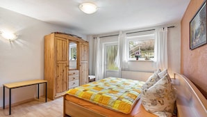 A bedroom with a bed, a wooden wardrobe, a small table, and a window with curtains. - Apartment "Heidi" with Mountain View, Private Garden and Wi-Fi (Rosenthal-Bielatal)