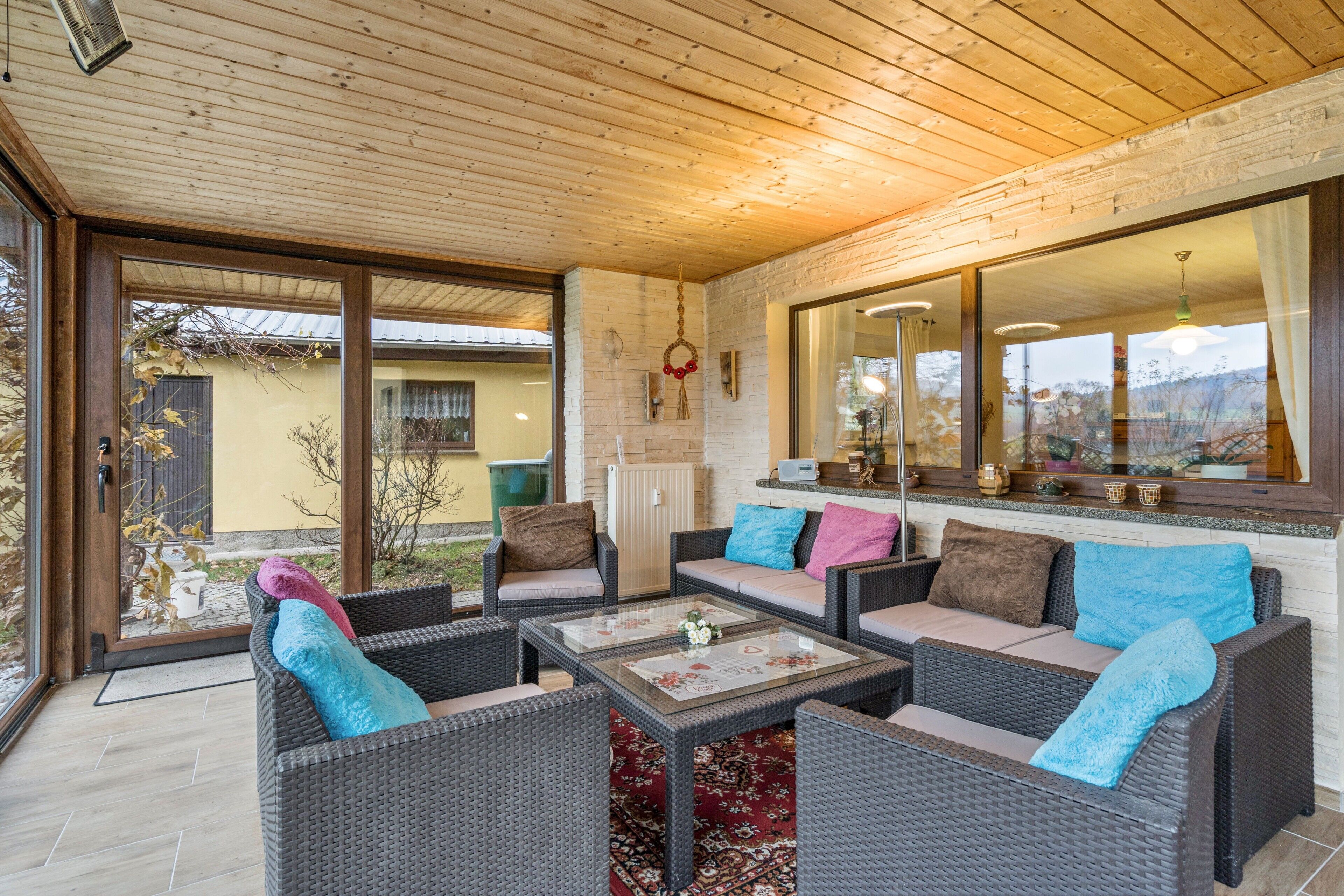 Ein überdachter Patio-Bereich mit Korbmöbeln, einem Glastisch und Blick ins Freie.