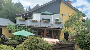 A two-story building with a balcony, outdoor seating, and potted plants. - Apartment "Heidi" with Mountain View, Private Garden and Wi-Fi (Rosenthal-Bielatal)