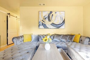 A living room with a grey tufted sofa set, a wooden coffee table, and a painting on the wall. - Charming 3-bedroom House with Office Space-Close to UF & Shands Hospital (Gainesville)
