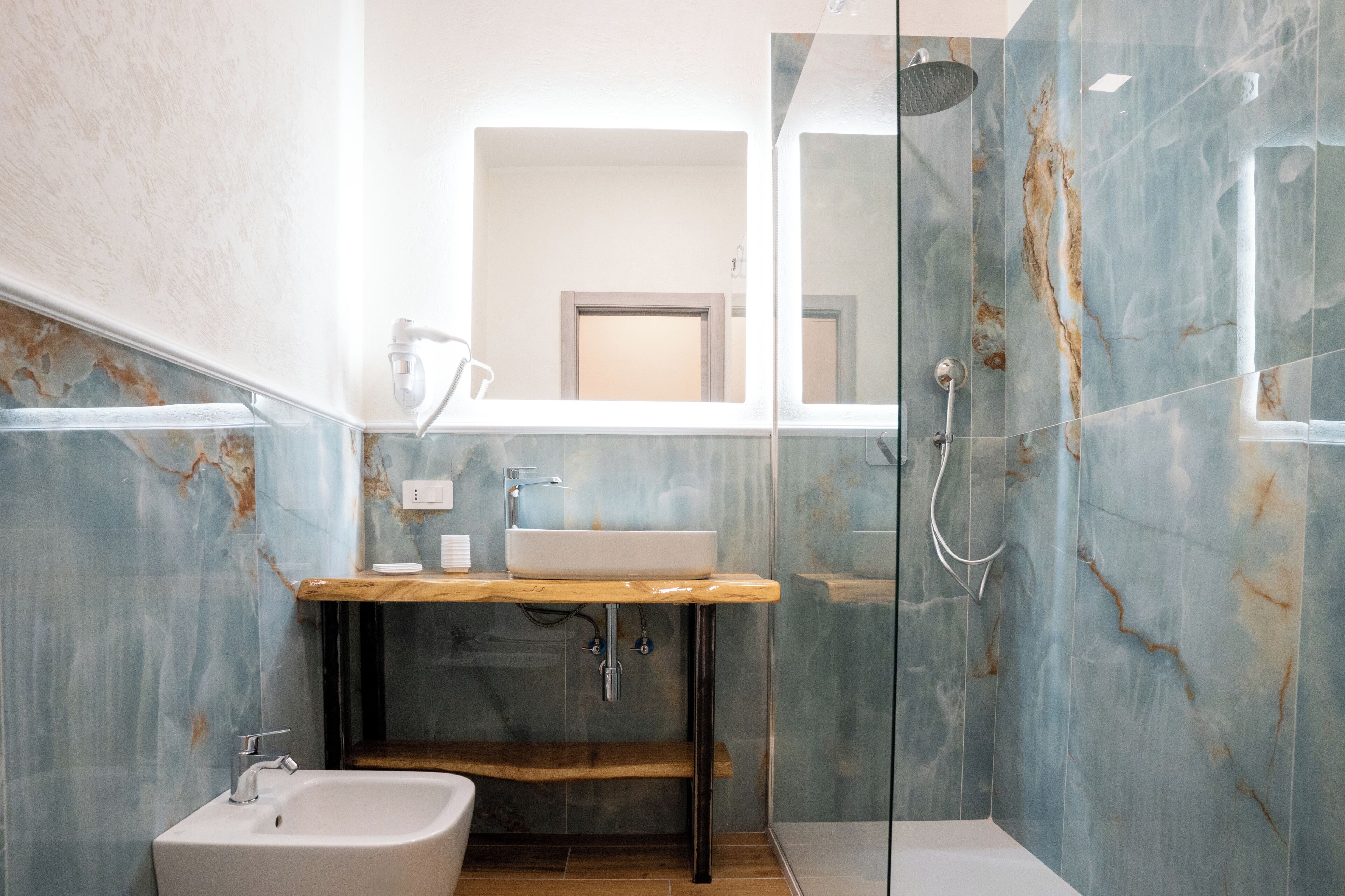 Un baño moderno con lavamanos de mármol, tocador de madera y ducha con cerramiento de vidrio.