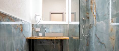Un baño moderno con lavamanos de mármol, tocador de madera y ducha con cerramiento de vidrio.
