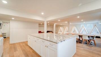 A spacious kitchen with white cabinets and a marble countertop, a dining area with a table and chairs, and a living area with a sofa and a TV.