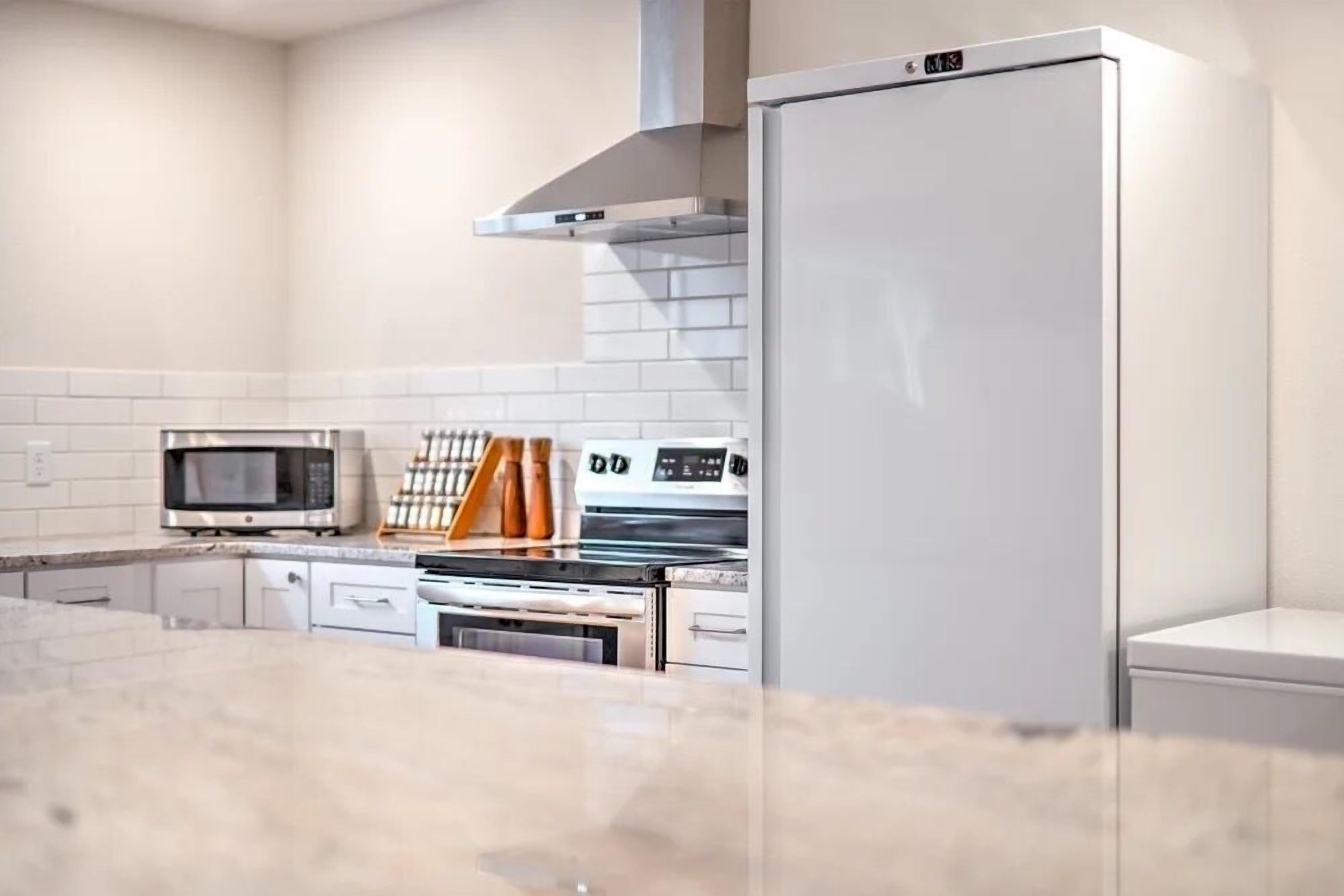 A modern kitchen with white cabinetry, a microwave, oven, and a refrigerator.
