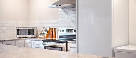 A modern kitchen with white cabinetry, a microwave, oven, and a refrigerator.
