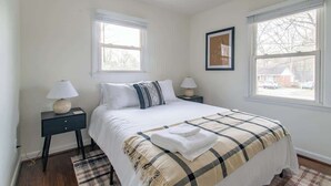 A bedroom with a bed, two nightstands, a window, and a framed picture on the wall. - Charming 3BR Home w/ Fenced Yard Near DT Raleigh (Raleigh)