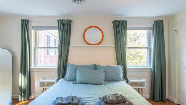 Um quarto com uma cama, duas almofadas, um espelho redondo e uma mesa de cabeceira.