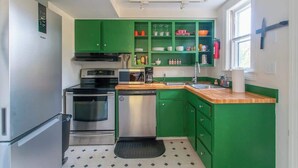 Uma cozinha compacta com armários verdes, eletrodomésticos de aço inoxidável e bancada de madeira.