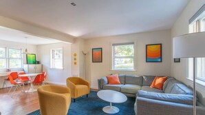 Uma sala de estar moderna com um sofá, poltronas, uma mesa de centro e uma área de jantar com cadeiras e uma mesa.