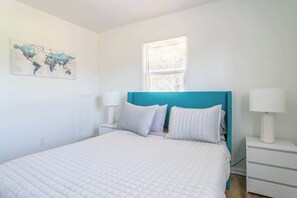 Un dormitorio con cama, un cuadro de un mapa mundial, una ventana y una mesita de noche con lámpara.